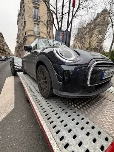 Mini Cooper noire sur la dépanneuse dans une rue haussmannienne de Paris
