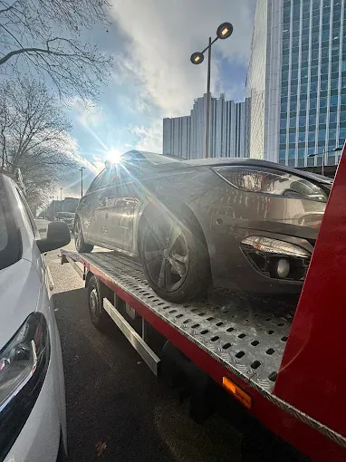 Voiture grise en panne remorquée sur le plateau rouge de la dépanneuse